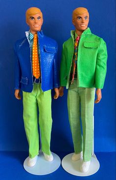 two male dolls dressed in green pants and blue jacket standing next to each other on a blue background