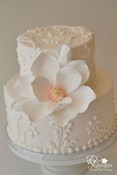 a white wedding cake with a large flower on the top and frosted icing