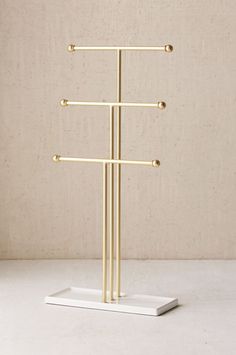 a three tiered gold metal rack on a white surface with beige wall in the background