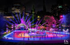 people skating on an ice rink in the city at night with colorful lights and fireworks