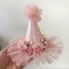 a hand holding a pink party hat with flowers and sequins on the top