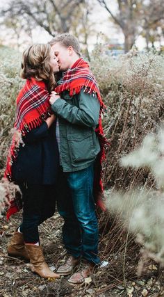 a man and woman kissing in the woods with a red plaid blanket on their shoulders