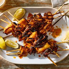 several skewers of food on a plate with lemon wedges and beer glasses