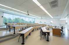 an empty classroom with desks and chairs in front of large windows on the wall