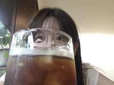 a woman holding up a glass with liquid in it and looking at the camera from behind