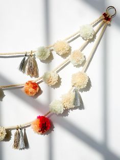 several pom poms hanging from a string on a white wall in the sunlight