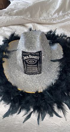 a white hat with black feathers and a jack daniels label on the front, sitting on top of a bed