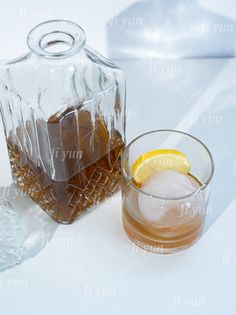 an iced beverage in a glass next to a decanter with ice and lemon wedges