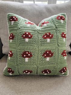 a green crocheted pillow sitting on top of a couch next to a window