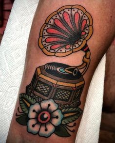 a tattoo with an old fashioned record player on it's left arm, and a flower in the foreground