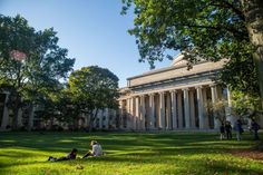 two people sitting on the grass in front of a large building with columns and pillars