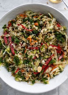 a white bowl filled with lots of food on top of a marble table next to utensils