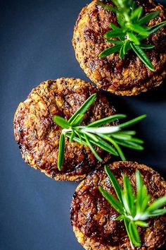 three meat patties with rosemary garnish on a black surface, top view