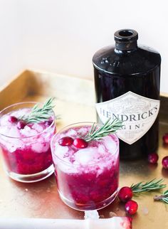 two glasses filled with ice and cranberries next to a bottle of liquor on a tray