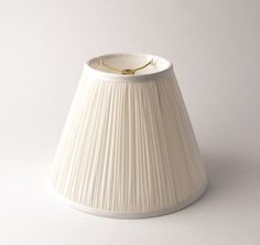 a white lamp shade sitting on top of a table next to a light bulb with a gold tip