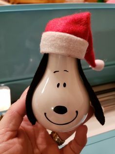 a person holding a snoopy christmas ornament with a santa hat on it