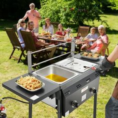 a man standing in front of an outdoor grill with food on it and people sitting at picnic tables behind him