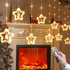 a person holding a remote control in front of a fireplace with christmas lights hanging from it