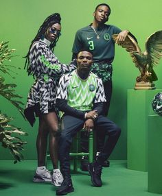 two men and a woman posing for a photo in front of green walls with an eagle statue