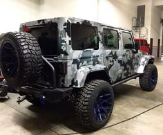 a camouflaged jeep is parked in a garage with blue rims and black tires