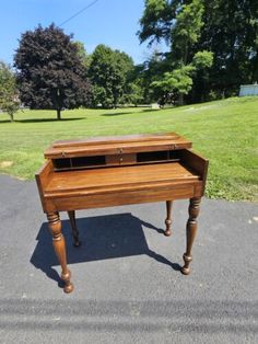 an old wooden desk sitting in the middle of a road with grass and trees behind it