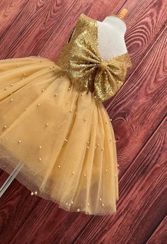 Our enchanting Knee Length flower girl dresses are sure to turn heads! This beautiful elegant sophisticated dress is handmade, the bodice consists of Gold Sequin, the back of the dress consists of an open V-back with a zipper. The big bow is detachable. The skirt consists of 4 layers of gold tulle with the top layer consisting with sowed in gold pearl beads. The fifth layer is made of lining with crinoline for fullness.  This dress is perfect for any occasion!  Dress Is Pictured with a petticoat Gold Color Dresses, Junior Dress, Gold Tulle, Haircuts For Long Hair With Layers, Bow Wedding, Elegant Sophisticated, Wedding Bows, Wedding Flower Girl, Sophisticated Dress