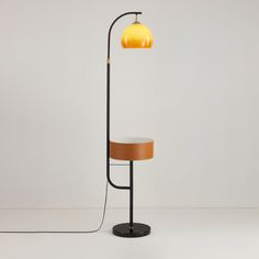 a floor lamp with a yellow shade on the top and a black stand underneath it