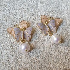 two pairs of butterfly shaped earrings on carpeted area with white and gold beads in the middle