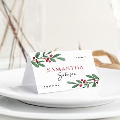 a place card is sitting on a white plate with red berries and greenery around it