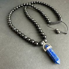 * This stunning pendant necklace features an 8mm Matte Black Onyx and black tourmaline stone with a Lapis Lazuli point. The combination of these stones creates a powerful and stylish accessory for men. * The necklace is adjustable, allowing for a perfect fit for any neck size ending with 6mm hematite beads.  The matte black finish of the Onyx and tourmaline stones adds a sleek and modern touch to the design. * The Lapis Lazuli point adds a pop of color and a touch of elegance to the overall look Black Pendant Necklace With Stones, Black Amulet Necklace With Natural Stones, Obsidian Necklace With 8mm Beads As Gift, Spiritual Obsidian Necklace With Gemstone, Spiritual Obsidian Gemstone Necklace, Black Crystal Pendant Necklace With Gemstone Beads, Obsidian Necklace With Gemstone Beads As Gift, Obsidian Gemstone Beads Necklace As Gift, Obsidian Gemstone Beads Necklace For Gift