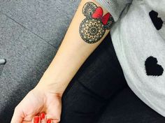 a woman's arm with a mickey mouse tattoo on her left wrist and red nail polish