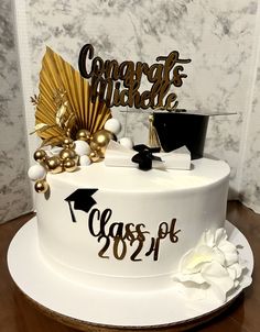 a white graduation cake with gold decorations and congratulations wishes on the top, sitting on a wooden table