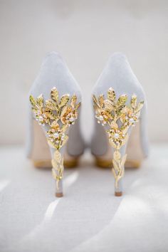 a pair of white high heels with gold flowers on the side and pearls in the heel