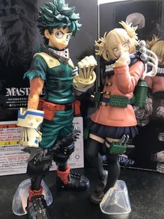 two anime figurines standing next to each other on a table with an advertisement in the background