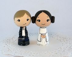 two small figurines are standing on a white doily, one is holding the other's hand