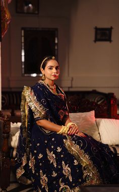 a woman sitting on top of a couch wearing a blue and gold sari dress