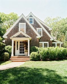 a house that is in the middle of some grass and bushes with trees around it