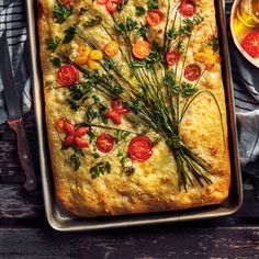 a square casserole with tomatoes and herbs on top, next to a glass of wine