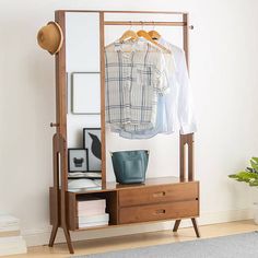 a coat rack with clothes hanging on it next to a rug and potted plant