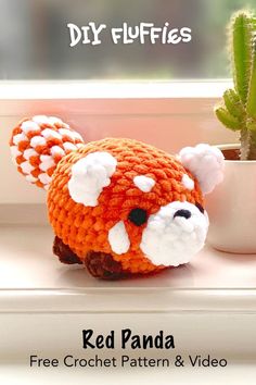 a crocheted red panda is sitting next to a potted cacti