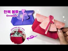 an origami envelope with pink ribbon and bow on it, being held by someone's hand