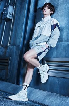 a boy is leaning against a wall with his legs crossed and wearing white tennis shoes