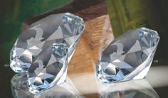 two clear crystal objects sitting next to each other on a wooden table with green leaves in the background