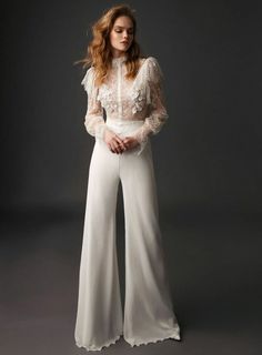 a woman in white is posing with her hands on her hips and wearing wide pants