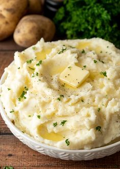 mashed potatoes with butter and parsley in a white bowl on a wooden table