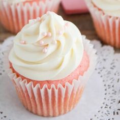 three cupcakes with white frosting and pink icing on a doily