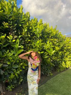 a woman standing in front of a bush with her hand on the top of her head