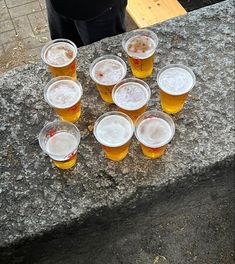 there are many glasses of beer sitting on the stone table top, ready to be served