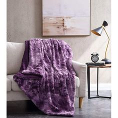 a couch with a purple blanket on top of it next to a table and lamp