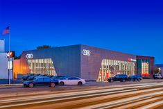 cars are parked in front of an audi dealership at night with lights streaking across the street